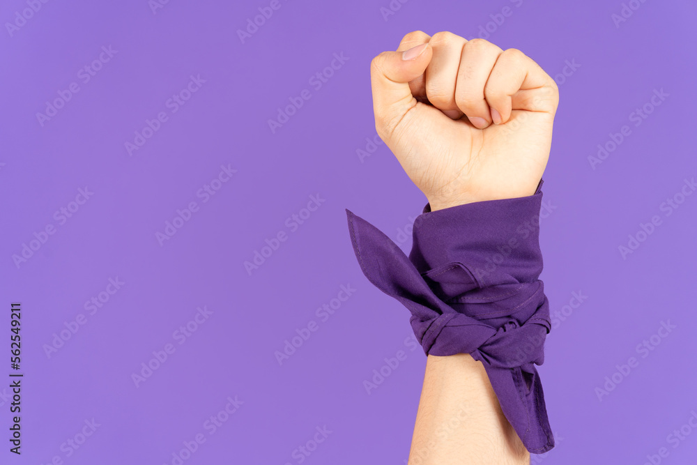 Closeup of closed fist and kerchief tied on wrist isolated on purple background. Feminism and protest concept with copy space - obrazy, fototapety, plakaty 