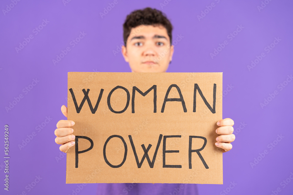 Hispanic teenager boy showing cardboard with feminist message isolated on purple background. Feminism and woman power concept Hispanic teenager boy showing cardboard with feminist message isolated on purple background. Feminism and woman power concept