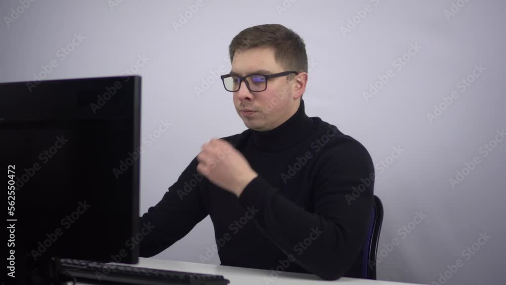 An IT specialist is sitting in the office at the computer and an idea came to him. The young man works in the office. An IT specialist is sitting in the office at the computer and an idea came to him. The young man works in the office.