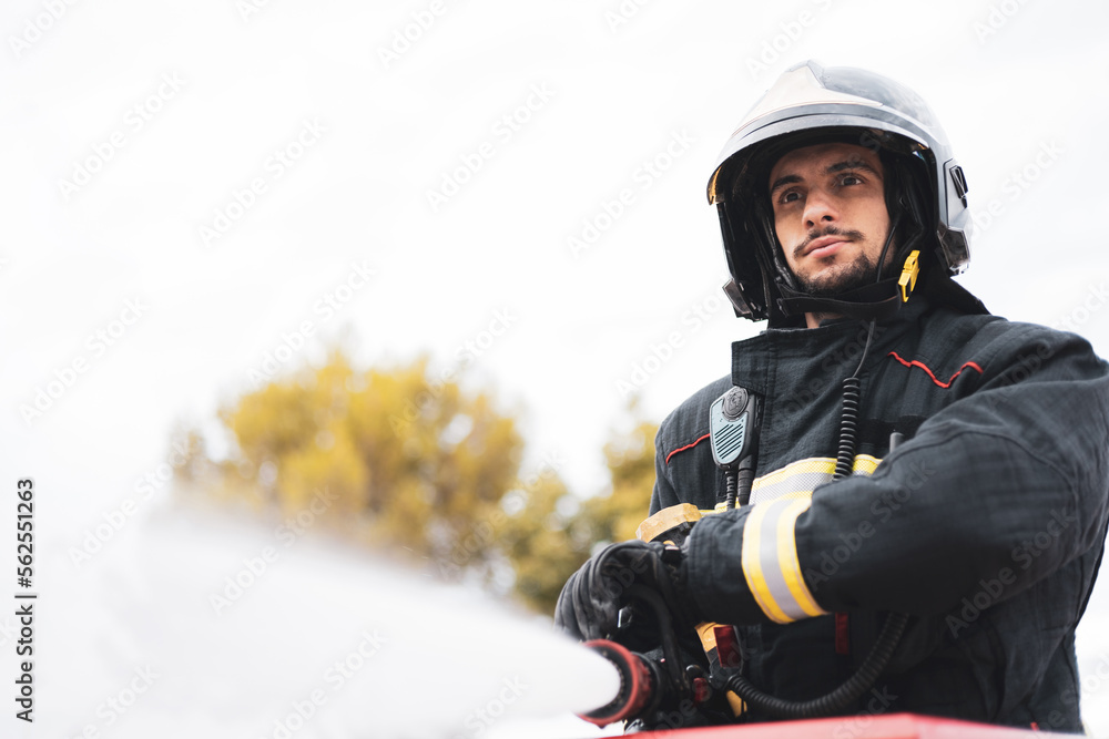 A young firefighter dressed in uniform uses the hose to put out a fire, emergency service. A young firefighter dressed in uniform uses the hose to put out a fire, emergency service.
