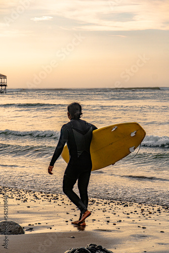 surfer on the beach under a beautiful sunset in front of the pier with big sea waves