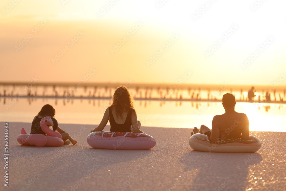 Happy summer family vacation. Silhouette of Mom, Dad and child daughter having fun together on seashore and sitting in floats on beautiful sunset. Fathers day, Mothers day, Baby day