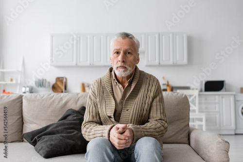 senior grey haired man with azheimers syndrome sitting on couch at home and looking at camera.