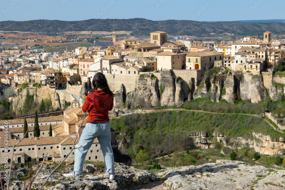 Portrait of woman tourist with photo camera hiking in hills in front of Cuenca hanging houses in Spain