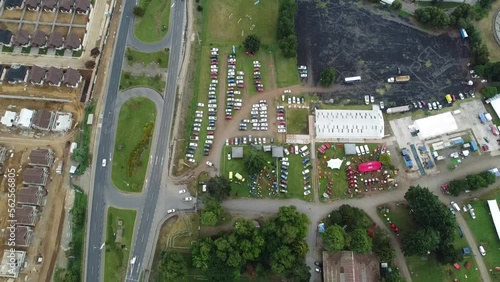 A look at the road, surrounded by a rural fair, where farm products are sold.
Cars drive in and out of town.