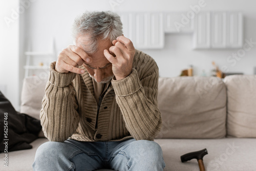 senior man with parkinson disease and trembling hands sitting with bowed head on couch at home. © LIGHTFIELD STUDIOS
