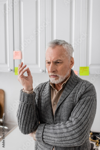 Fotografie thoughtful man with alzheimer disease standing near blurred sticky notes in kitchen