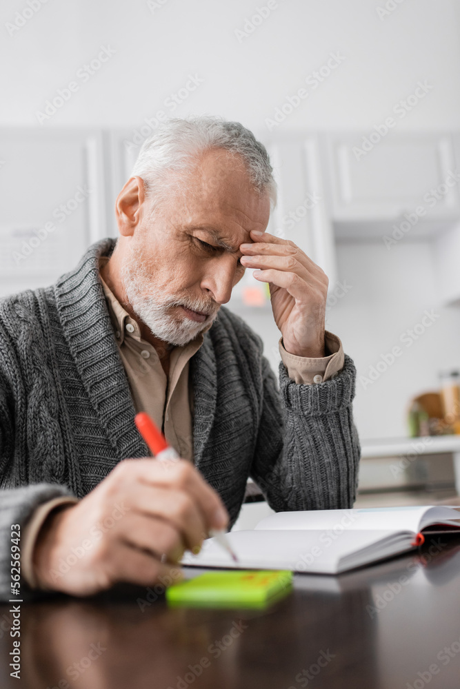 thoughtful man touching forehead while sitting with felt pen near sticky notes and empty notebook. thoughtful man touching forehead while sitting with felt pen near sticky notes and empty notebook.