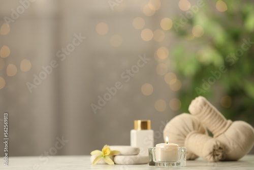 Composition with herbal bags and burning candle on white table against blurred festive lights, space for text
