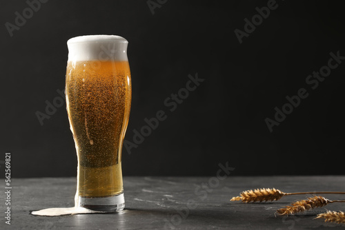 Canvas Print Glass of beer and spikes on black table. Space for text