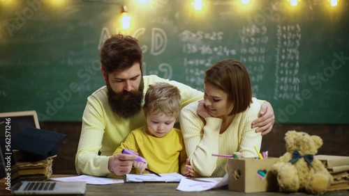 Young family studying. Family with little child boy reading book In playroom class. Happy cute clever boy. Child ready to answer with chalkboard on background. Ready for school. photo