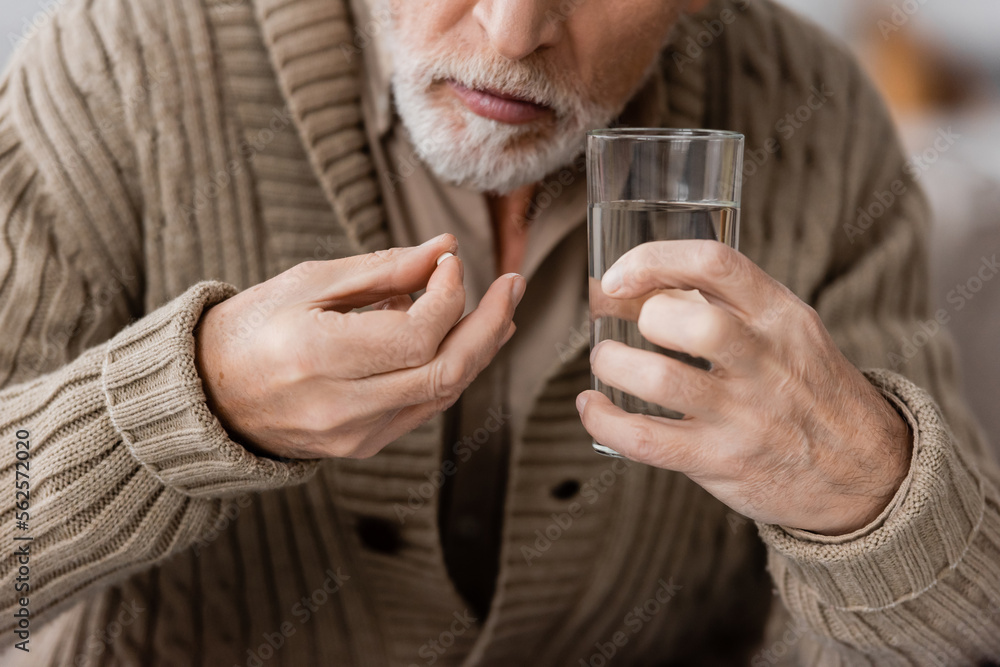 partial view of senior man with parkinson disease holding pill and glass of water in trembling hands. partial view of senior man with parkinson disease holding pill and glass of water in trembling hands.