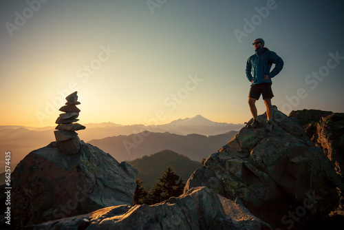 A hiker stands on a large rock, opposite the summit cairn or Sauk Mountain.