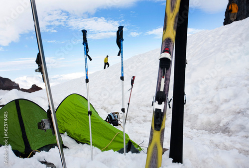 A climber walks the ridgeline with two bivy sacks and skis in the foreground. photo