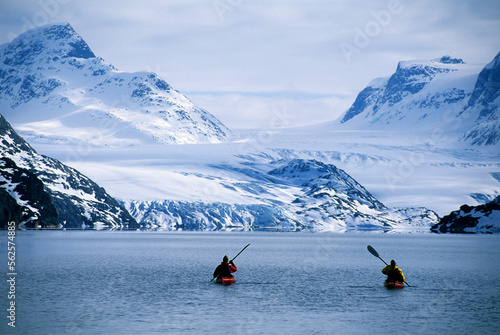 Two people sea kayaking near snowy coast of Greenland.