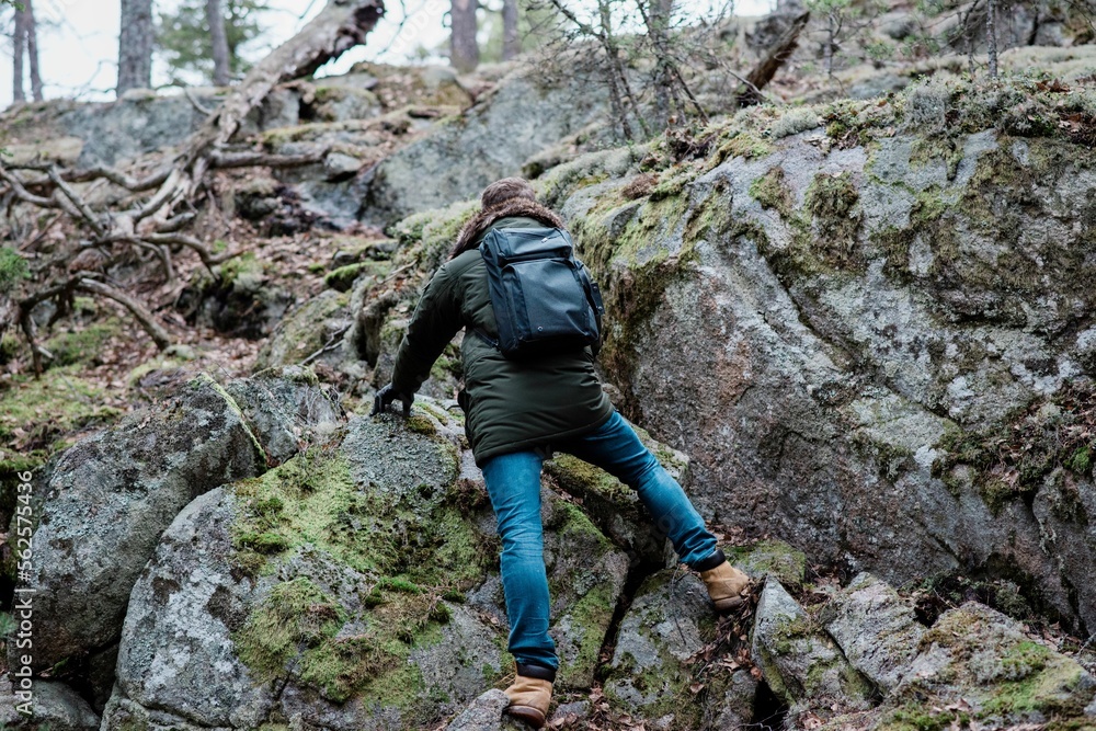 man climbing a rock whilst hiking in a forest in winter man climbing a rock whilst hiking in a forest in winter