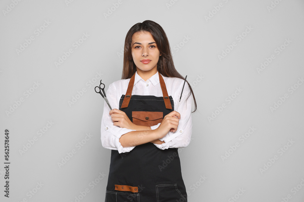 Portrait of happy hairdresser with professional scissors and comb against light grey background Portrait of happy hairdresser with professional scissors and comb against light grey background