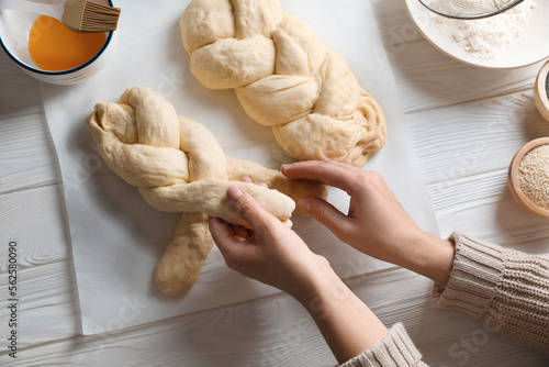 Woman cooking braided bread at white wooden table in kitchen, top view. Traditional Shabbat challah photo