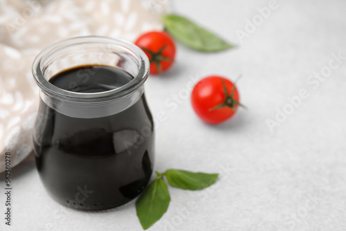 Glass jar with balsamic vinegar, basil and tomatoes on white table, closeup. Space for text