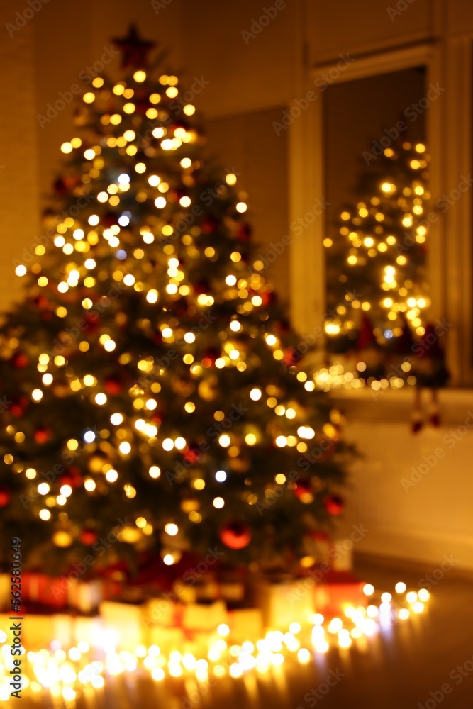 Beautiful Christmas tree, gifts and festive lights near window in room, blurred view Beautiful Christmas tree, gifts and festive lights near window in room, blurred view