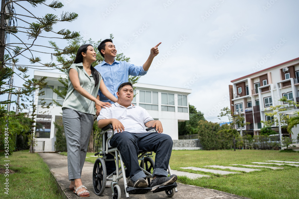Asian attractive family walking with young son on wheelchair in garden.