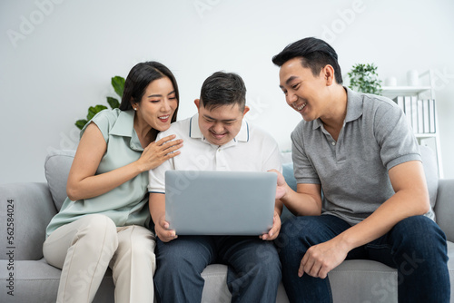 Asian happy family, parents using laptop with young son in living room.
