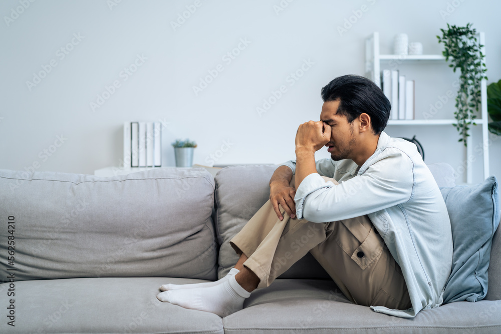 Asian young upset depressed man sitting alone in living room at home. Asian young upset depressed man sitting alone in living room at home.