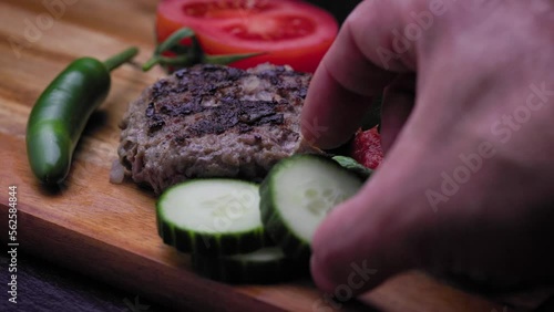 Decorating traditional Bulgarian dish with slices of cucumber. Kufte, chili pepper, tomato slice and lutenica dipping sauce on a lettuce leaf. photo