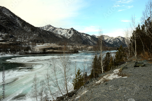 The frozen bed of a beautiful river flowing through a winter valley surrounded by snow-capped mountains on a clear December day.