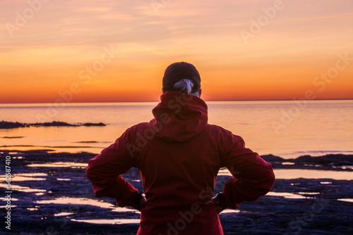 Rear view of woman admiring beautiful sunset over water.