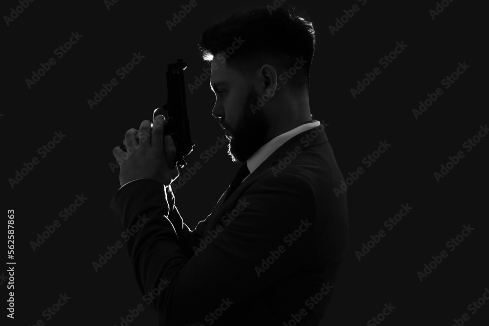 Silhouette of young man in suit with gun on dark background Silhouette of young man in suit with gun on dark background