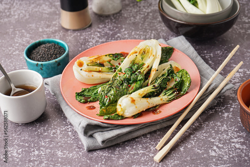 Plate of tasty stewed pak choi cabbage with soy sauce and chopsticks on grunge background photo