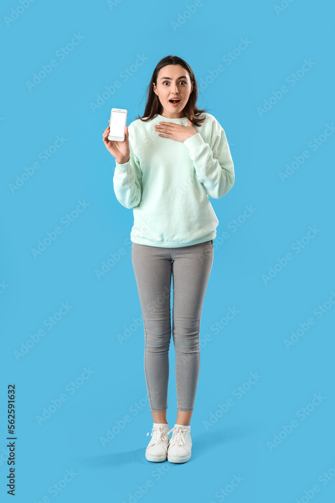 Surprised young woman with mobile phone on blue background Surprised young woman with mobile phone on blue background