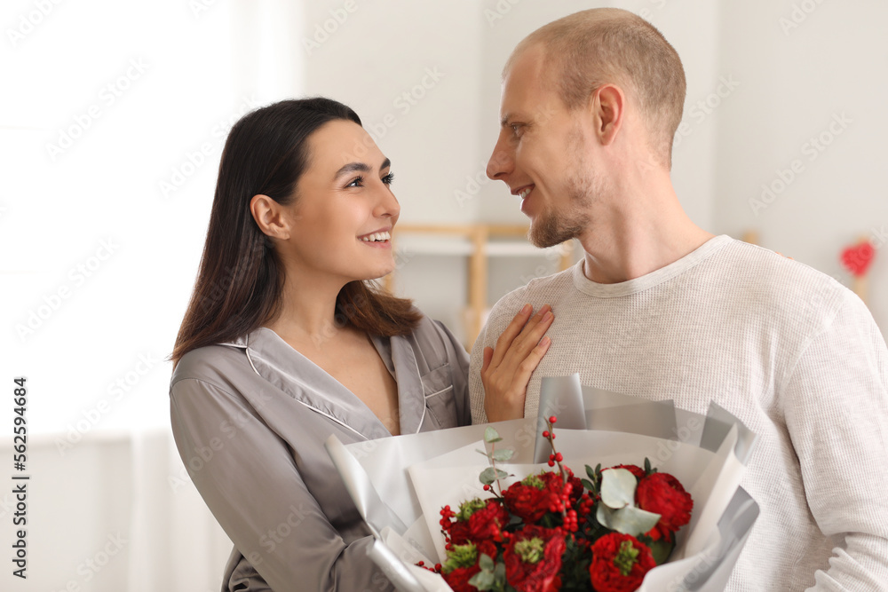 Young couple with bouquet of flowers in bedroom on Valentine's Day Young couple with bouquet of flowers in bedroom on Valentine's Day