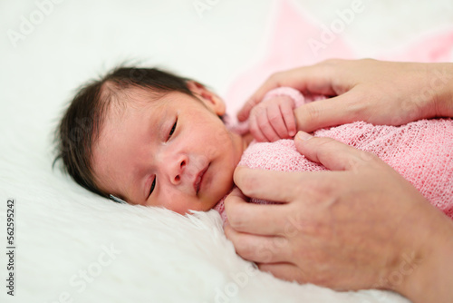 newborn baby wrap in blanket and parent hands putting on bed