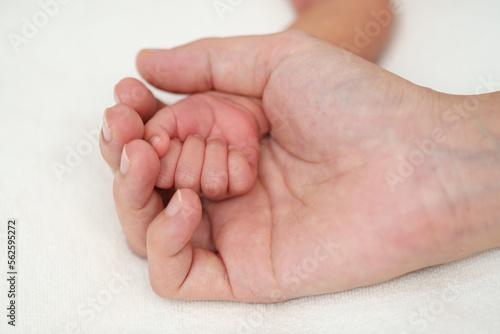 mother holding newborn baby hand on bed