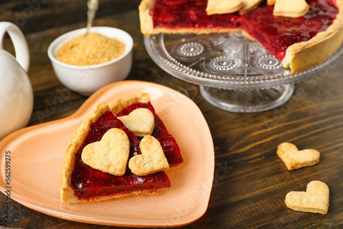 Heart-shaped plate with pieces of sweet strawberry pie, cookie hearts and bowl of brown sugar on wooden table