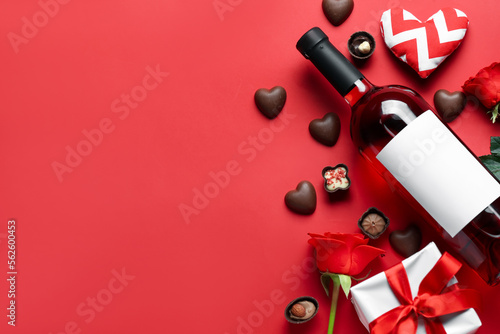 Bottle of wine, chocolate candies, rose flowers and gifts on red background. Valentine's Day celebration