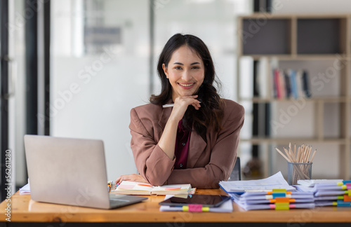Freelancer Happy business Asian woman in knitwear taking notes at laptop sitting at desk office, finance concept.
