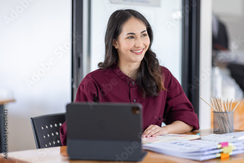 Freelancer Happy business Asian woman in knitwear taking notes at laptop sitting at desk office, finance concept.
