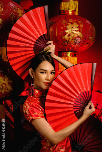 asian woman in tradional chinese red costume holding chinese fan with background of chinese lantern for chinese new year celebration