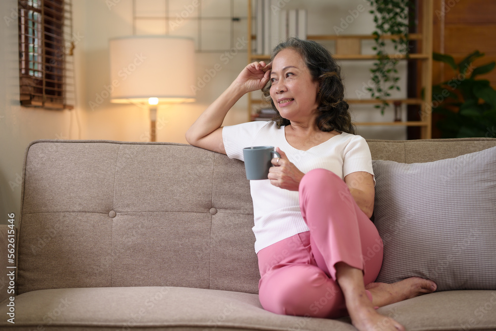 Senior Asian woman sitting and relaxing on the sofa at home drinking coffee in a relaxed and happy way. Senior Asian woman sitting and relaxing on the sofa at home drinking coffee in a relaxed and happy way.