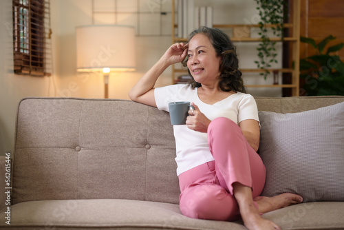 Senior Asian woman sitting and relaxing on the sofa at home drinking coffee in a relaxed and happy way.