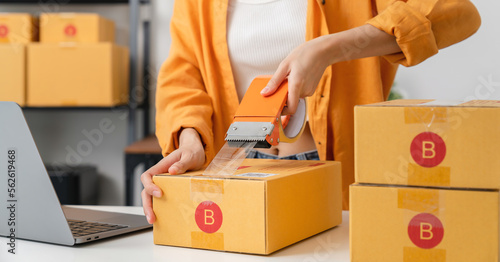 Startup small business, Young Asian woman owner using adhesive tape, packing carton parcel box working at the home office, seller prepares the delivery. photo