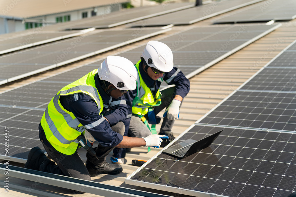 Well-equipped worker in protective clothing working and examining solar panels on a photovoltaic rooftop plant. Concept of maintenance and installation of solar station. Well-equipped worker in protective clothing working and examining solar panels on a photovoltaic rooftop plant. Concept of maintenance and installation of solar station.