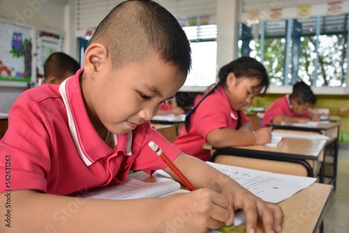 Early elementary school children in Thai student uniform are intending to make work sheets in the classroom.