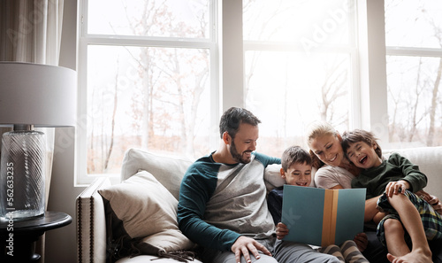 Books, reading and couple with children on couch for storytelling time in living room of happy home. Love, learning and growth, woman and man with kids, book and fantasy story smile on sofa together.