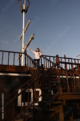 A girl with long hair stands on the deck of a ship. Beautiful warm sunset.