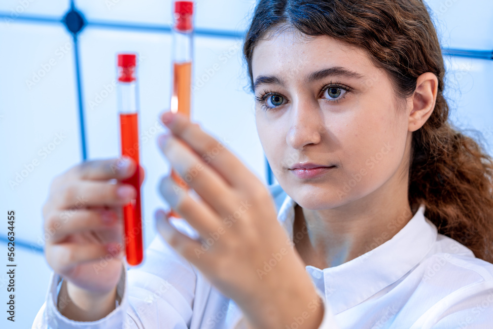 girl laboratory assistant compares the contents of two test tubes in a