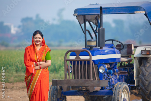 Indian rural woman standing near new tractor and giving happy expression.